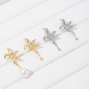 Puede incluir: Un par de pendientes florales de oro y plata con una perla colgante en un lado. Los pendientes presentan un delicado diseño floral con una cadena colgante.
