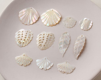May include: A collection of white iridescent shell and leaf shaped charms with holes for jewelry making. The charms are arranged on a white plate.