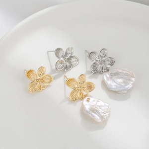 May include: A pair of earrings featuring a delicate flower design. One earring is gold with a white pearl drop, the other is silver with a white pearl drop.