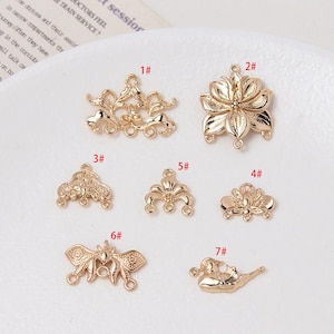 May include: Seven gold-toned metal connector charms with different designs, including a flower, a butterfly, and a stylised leaf. Each charm has three loops for attaching to jewellery or other crafts.