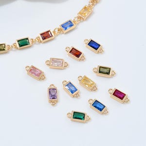 May include: Gold-toned jewelry components with rectangular, multi-colored gemstones. The gemstones are in shades of red, blue, green, yellow, pink, and purple. A gold chain with similar gemstones is also visible.