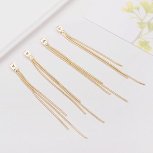 May include: Four pairs of gold-toned dangle earrings with multiple chain strands. The earrings are simple and elegant.