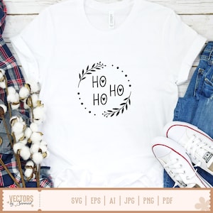 Puede incluir: Una camiseta blanca de manga corta con un estampado gr&aacute;fico negro en el pecho. El dise&ntilde;o consiste en el texto HO HO HO con corazones en el centro de las letras O, encerrado en un marco circular de hojas y peque&ntilde;os puntos.