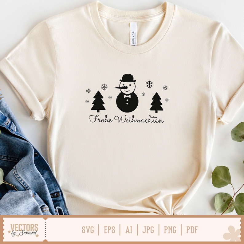 Puede incluir: Una camiseta de manga corta de color crema con un gr&aacute;fico negro de un mu&ntilde;eco de nieve con bomb&iacute;n y pajarita, flanqueado por dos pinos y varios copos de nieve. Debajo del gr&aacute;fico, el texto dice Frohe Weihnachten en una tipograf&iacute;a negra.
