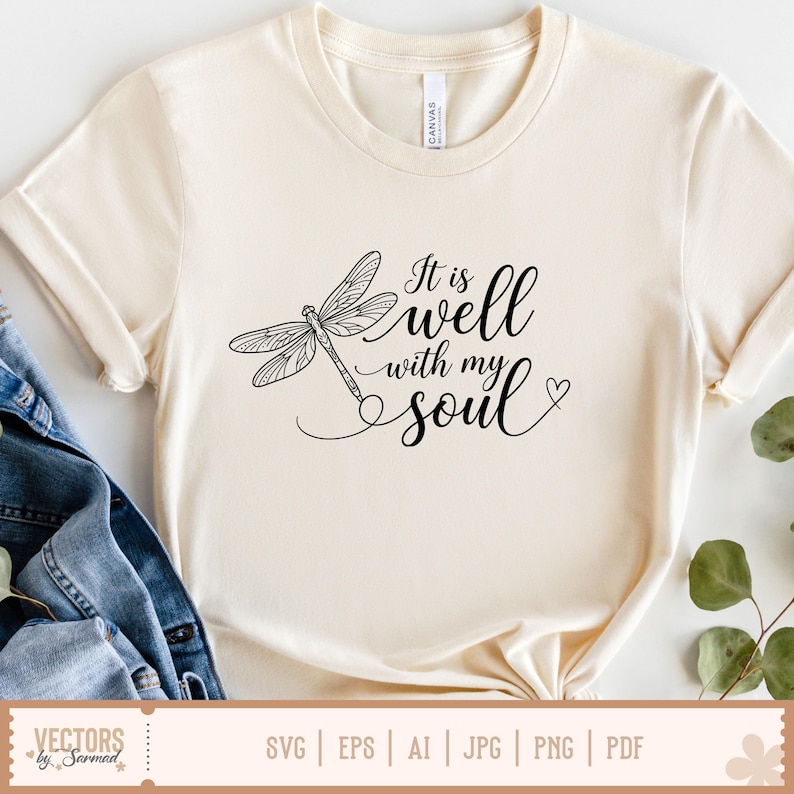 Puede incluir: Camiseta color crema con una ilustraci&oacute;n de lib&eacute;lula negra y la frase "It is well with my soul" en fuente cursiva. El dise&ntilde;o incluye un peque&ntilde;o coraz&oacute;n. La camiseta est&aacute; hecha de un material suave.