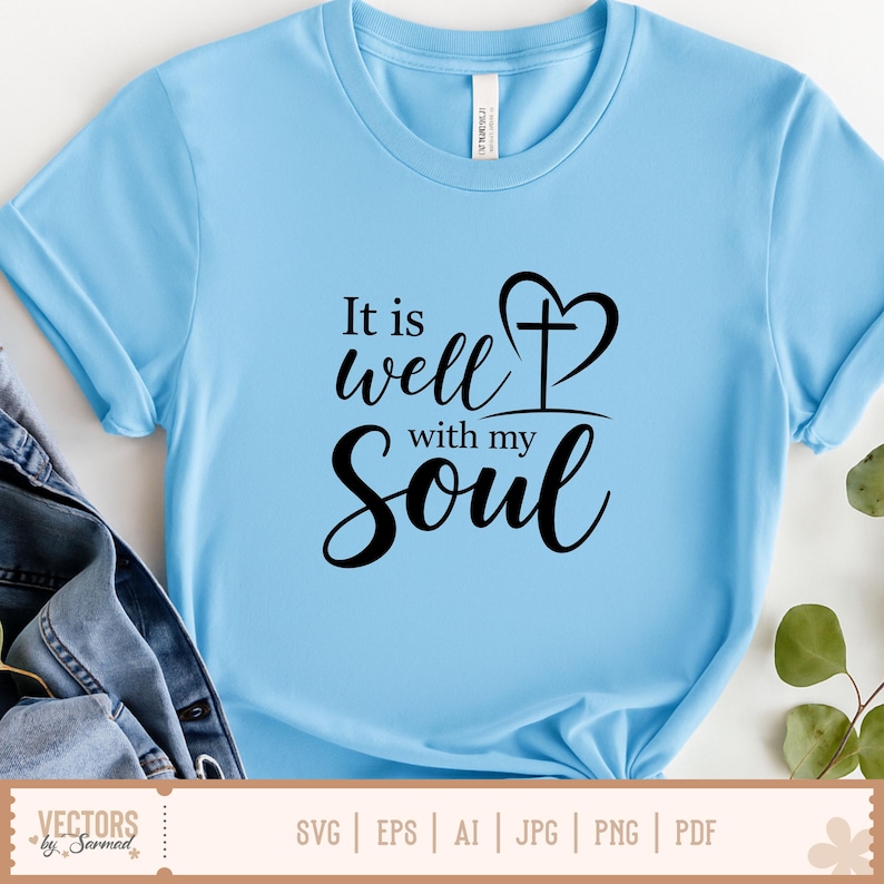 Puede incluir: Camiseta azul claro con la frase "It is well with my Soul" en escritura negra. El dise&ntilde;o incluye una cruz en forma de coraz&oacute;n. La camiseta es de material suave y tiene mangas cortas.