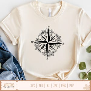 以下が含まれることがあります： クリーム色の半袖Tシャツ。中央には、円形のフラワーリースに囲まれた黒いコンパスローズ（羅針盤）のグラフィックが描かれています。方位はN、S、E、Wの文字で示されています。クルーネックの標準的なフィット感のTシャツです。