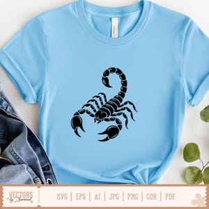 Op de afbeelding: Lichtblauw T-shirt met een zwarte schorpioenafbeelding. De schorpioen is gecentreerd en is een gedetailleerde illustratie. Het shirt heeft korte mouwen en een ronde hals. De onderkant van de afbeelding toont de tekst "SVG | EPS | AI | JPG | PNG | CDR | PDF".
