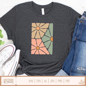 Op de afbeelding: Donkergrijs t-shirt met een rechthoekig bloemenontwerp in perzik, beige en groen met oranje centra. Het shirt wordt gecombineerd met een blauwe jeans en witte sneakers. Het woord "CANVAS" staat op het label van het shirt.