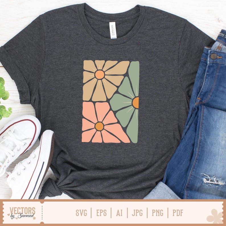 Op de afbeelding: Donkergrijs t-shirt met een rechthoekig bloemenontwerp in perzik, beige en groen met oranje centra. Het shirt wordt gecombineerd met een blauwe jeans en witte sneakers. Het woord "CANVAS" staat op het label van het shirt.