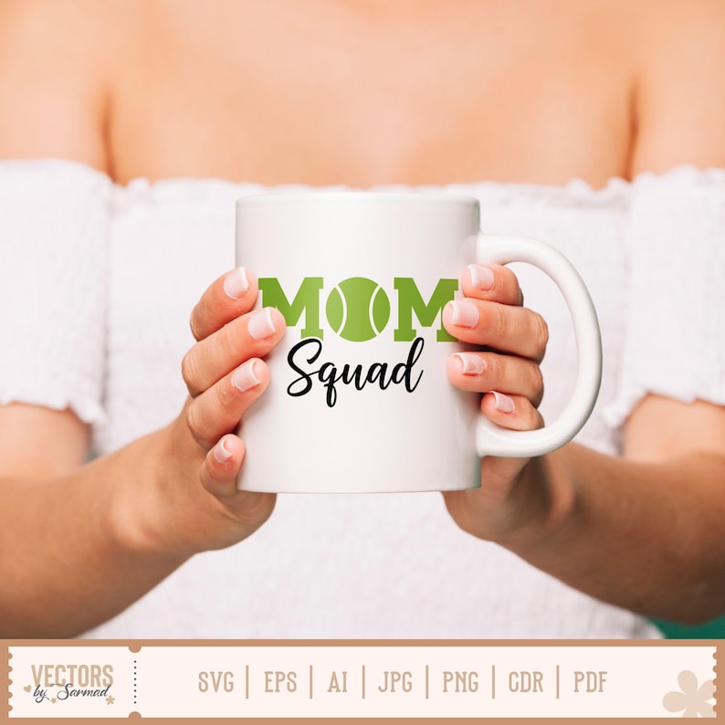 May include: White ceramic mug with the words "MOM Squad" in green and black. The "O" in "MOM" is a green tennis ball. The mug is held by a person wearing a white off-the-shoulder top.