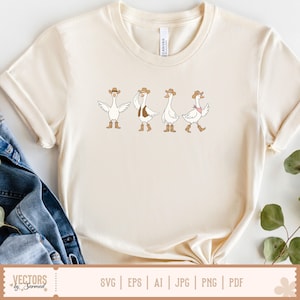 May include: A cream-coloured short-sleeve t-shirt featuring a graphic of four white geese wearing brown cowboy hats and boots. One goose has wings spread, one wears a brown waistcoat, and one wears a pink neckerchief. The shirt has a crew neckline.