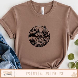 以下が含まれることがあります： 茶色のクルーネックTシャツで、黒い円形のグラフィックプリントが施されています。デザインは、灯台、山、松の木、海の波を含む風景の中に配置されたコンパスローズを描いています。Tシャツは標準的な半袖のカットです。