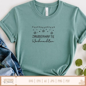 Puede incluir: Una camiseta de manga corta en color verde azulado polvoriento con un gr&aacute;fico negro de adornos navide&ntilde;os colgantes, estrellas y luces. Debajo del gr&aacute;fico, el texto dice ZAUBERHAFTE Weihnachten en una combinaci&oacute;n de letras negritas y cursivas.