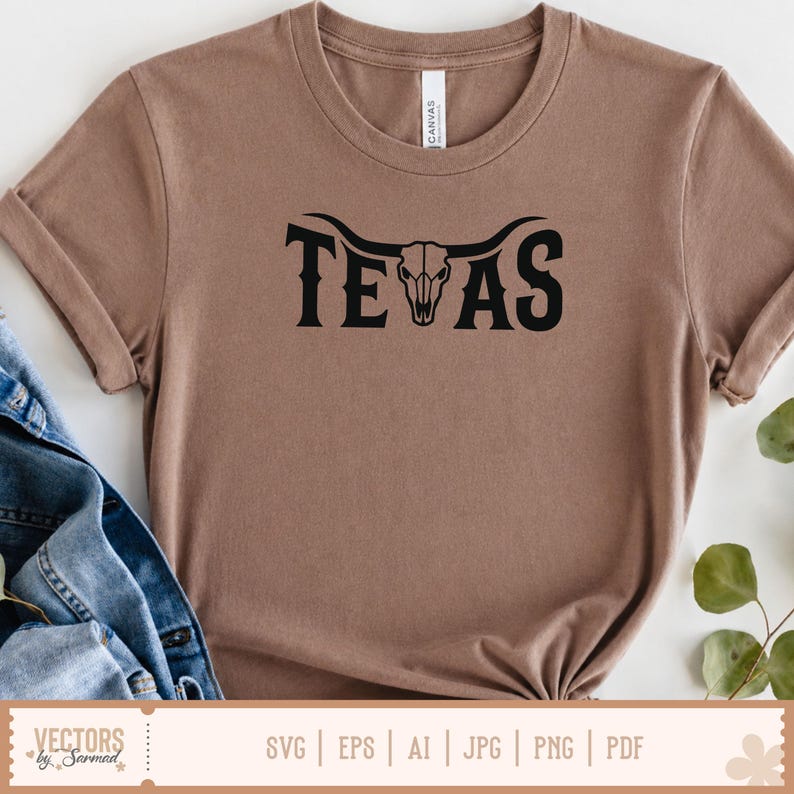May include: A brown t-shirt with the word "TEXAS" in black, featuring a longhorn skull design. The shirt is folded, with a denim jacket visible on the side. The word "CANVAS" is printed on the tag.