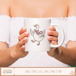 May include: A white ceramic mug featuring a graphic illustration of a white goose with orange feet and beak, wearing a light pink ribbon bow around its neck. The goose is depicted with its wings spread out as if walking or dancing on the mug surface.