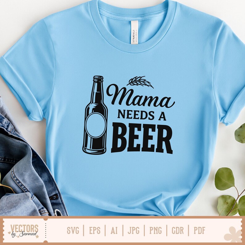May include: Light blue t-shirt with the text "Mama NEEDS A BEER" in black. A black beer bottle graphic is on the left side of the text. The shirt is made of a soft material and has rolled-up sleeves.