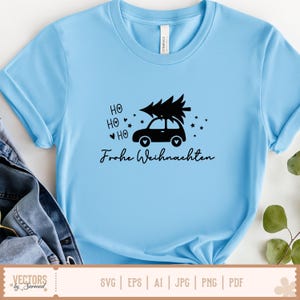 Puede incluir: Una camiseta azul claro con un gr&aacute;fico negro de un coche que lleva un &aacute;rbol de Navidad en el techo. El dise&ntilde;o incluye el texto "HO HO HO" con corazones, peque&ntilde;as estrellas y la frase "Frohe Weihnachten" escrita en letra cursiva.