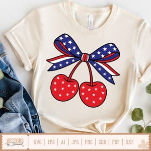 Puede incluir: Una camiseta blanca con un lazo rojo, blanco y azul con estrellas y dos cerezas rojas con estrellas blancas. El lazo está atado en el centro de las cerezas.
