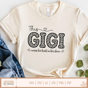 Pu&ograve; includere: T-shirt color crema con la scritta "This GIGI" in corsivo nero e stampa leopardata. La frase "wears her heart on her sleeve" &egrave; sotto. La maglietta ha le maniche arrotolate ed &egrave; abbinata a una giacca di jeans.