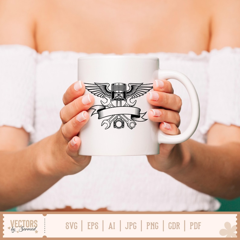May include: White ceramic mug featuring a black graphic of an engine piston with wings, wrenches, and a banner. The mug has a curved handle and is held by a person. The mug is a great gift for mechanics and car enthusiasts.