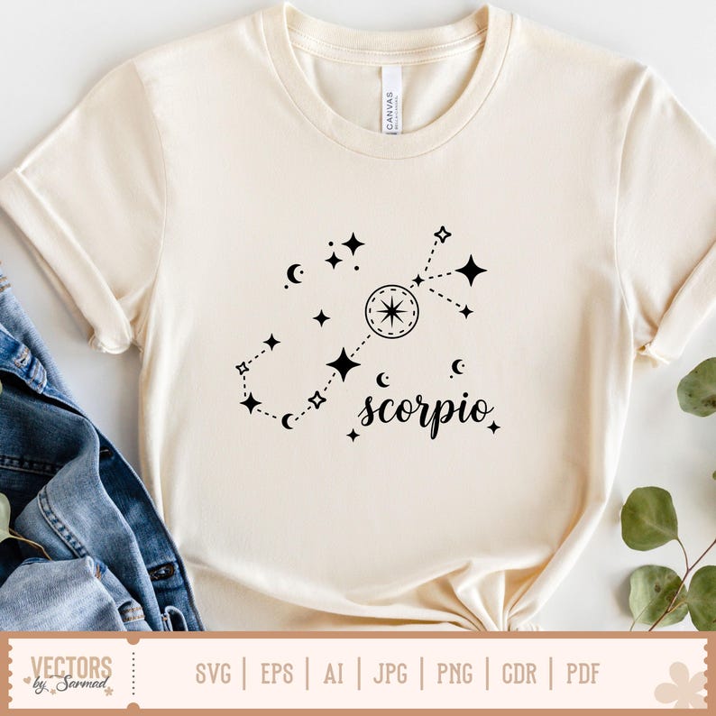 Op de afbeelding: Cr&egrave;mekleurig T-shirt met een zwart Schorpioen sterrenbeeld ontwerp. Het ontwerp bevat sterren, manen en het woord "scorpio" in een stijlvol lettertype. Het shirt is gemaakt van zacht materiaal.