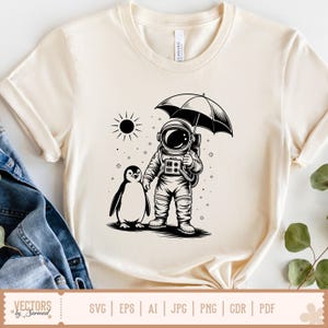 May include: Cream-colored t-shirt featuring a black and white illustration of an astronaut holding an umbrella, walking with a penguin. A sun graphic is in the background. The shirt has a crew neck and short sleeves. The bottom of the shirt has the text "VECTORS by Sarmad".