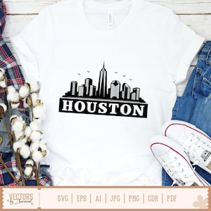 Peut inclure: T-shirt blanc avec un motif noir et blanc de l'horizon de Houston et le mot "HOUSTON". Le t-shirt est associ&eacute; &agrave; un jean bleu et des baskets blanches. Le motif comprend des oiseaux volant au-dessus de la ville.