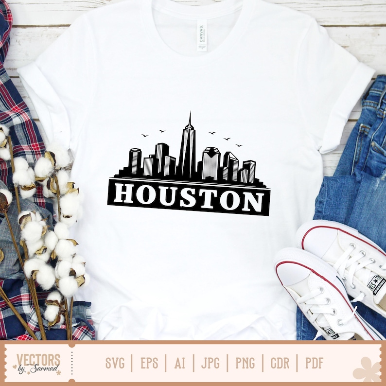 Peut inclure: T-shirt blanc avec un motif noir et blanc de l'horizon de Houston et le mot "HOUSTON". Le t-shirt est associ&eacute; &agrave; un jean bleu et des baskets blanches. Le motif comprend des oiseaux volant au-dessus de la ville.