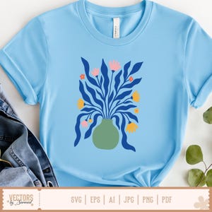 Op de afbeelding: Lichtblauw T-shirt met een bloemenontwerp. De afbeelding bevat een groene vaas met blauwe bladeren, roze en gele bloemen. De tekst "VECTORS by Sarmad" en bestandstype-opties staan onderaan.