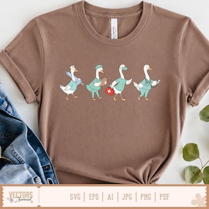 May include: A brown short-sleeved t-shirt featuring a graphic of four white geese dressed as medical professionals. The geese are depicted wearing teal scrubs, surgical caps, and masks, while carrying a syringe, clipboard, first aid kit, and stethoscope.
