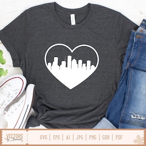 Peut inclure: T-shirt gris fonc&eacute; avec un motif blanc en forme de c&oelig;ur contenant une silhouette de ville. Le t-shirt est associ&eacute; &agrave; un jean bleu et des baskets blanches. Le bas de l'image contient le texte "VECTORS by Sarmad" et des options de type de fichier.