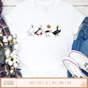 May include: A white t-shirt featuring a graphic of four geese in Halloween costumes: one as a ghost, one as a vampire with a red-lined cape, one with a pumpkin head, and one as a skeleton. The geese are arranged in a horizontal line across the chest.