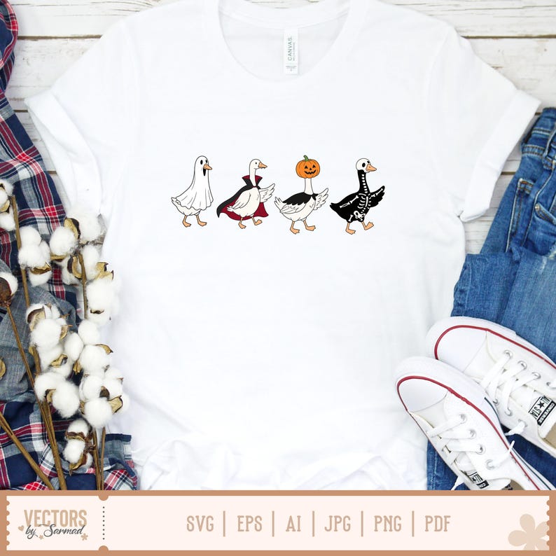 May include: A white t-shirt featuring a graphic of four geese in Halloween costumes: one as a ghost, one as a vampire with a red-lined cape, one with a pumpkin head, and one as a skeleton. The geese are arranged in a horizontal line across the chest.