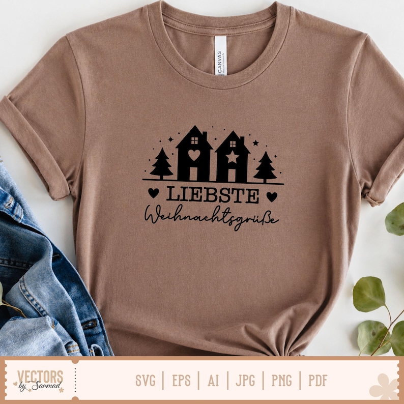 Puede incluir: Una camiseta de cuello redondo color canela con un gr&aacute;fico negro de dos casas, dos pinos y estrellas. La casa de la izquierda tiene un coraz&oacute;n y la de la derecha una estrella. Debajo del gr&aacute;fico aparece el texto "LIEBSTE" y "Weihnachtsgr&uuml;&szlig;e".