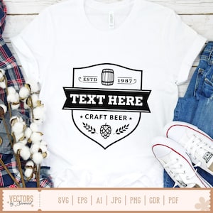 May include: White t-shirt with a black graphic design. The design includes the text "TEXT HERE", "CRAFT BEER", a barrel, and the year "1987". The shirt is paired with blue jeans and white sneakers.