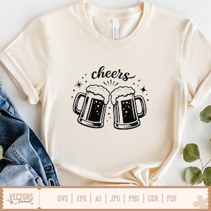 May include: Cream-colored t-shirt featuring a black graphic of two beer mugs with foamy tops, and the word "cheers" above them. The design includes stars and decorative elements. The shirt is made of a soft material.