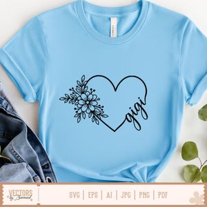 Pu&ograve; includere: T-shirt azzurra con un design a cuore nero con dettagli floreali e la scritta "gigi" in corsivo. La maglietta &egrave; realizzata in materiale morbido. La parte inferiore dell'immagine include il testo "SVG | EPS | AI | JPG | PNG | PDF".