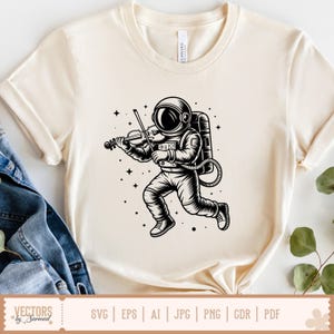 May include: Cream-colored t-shirt featuring a black and white illustration of an astronaut playing a violin while running. The design includes stars and a space theme. The shirt has short sleeves and a round neckline.