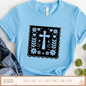 May include: Pale blue t-shirt with a black square design featuring a cross, flowers, hearts, and leaves. The shirt has short sleeves and a crew neck. The design is centered on the front. The shirt is made of a soft material.