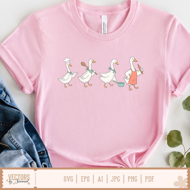 May include: A light pink t-shirt featuring a graphic illustration of four white geese in a row. The geese are depicted with cooking accessories including a chef hat, a wooden spoon, a green neckerchief, a cooking pot, and a coral-coloured apron.