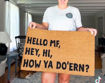 Könnte beinhalten: Eine braune Kokosmatte mit dem Text "HELLO MF, HEY, HI, HOW YA DO'ERN?" in schwarzen Buchstaben.