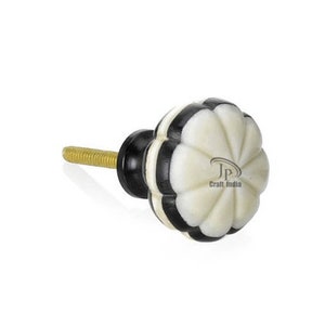 May include: A decorative cabinet knob with a white, black, and gold colour scheme. The knob has a flower-like design with alternating white and black segments. The threaded post is gold-coloured.