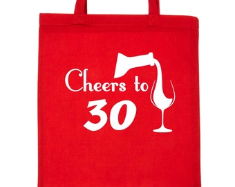 以下が含まれることがあります： ワインボトルがワイングラスに注がれているグラフィックと、「Cheers to 30」という白い文字が書かれた赤いトートバッグ。