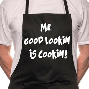 Pode incluir: Avental preto com texto branco que diz "Mr. Good Lookin' is Cookin!"