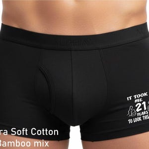 May include: Black boxer briefs featuring a wide waistband with the embossed text ALPHA. The fabric is an ultra soft cotton bamboo mix. The right leg displays white text that reads IT TOOK ME 21 YEARS TO LOOK THIS GOOD with two thumbs up icons.