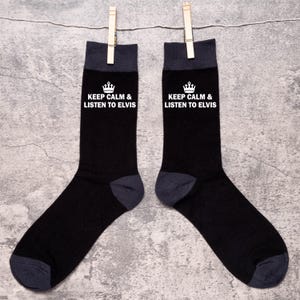 Puede incluir: Un par de calcetines negros con una corona blanca y el texto "Keep Calm & Listen to Elvis" en cada calcetín.