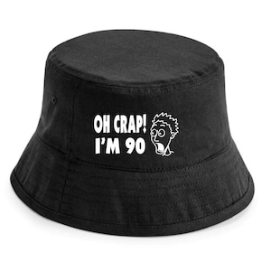 May include: Black bucket hat with white text that reads "OH CRAP! I'M 90" and a cartoon image of a surprised person.
