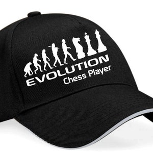 Puede incluir: Gorra de béisbol negra con un diseño blanco de un tablero de ajedrez y la evolución del hombre con el texto "EVOLUTION Jugador de ajedrez".