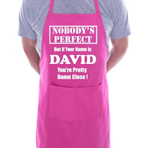 Puede incluir: Delantal rosa con un bolsillo blanco y el texto "Nobody's Perfect But if Your Name is DAVID You're Pretty Damn Close!"